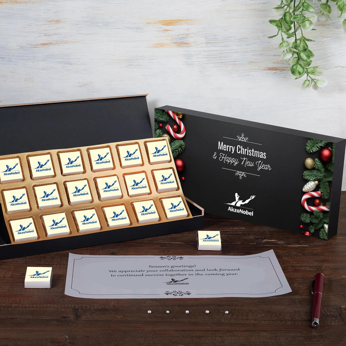 Straight view of 18 square dark chocolates with personalized wrappers inside a premium black gift box.